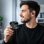 A man wearing a black wireless earbud in his ear while holding an open black wireless earbud charging case. He is sitting in a modern office or home office environment with a gray chair and blurred background.